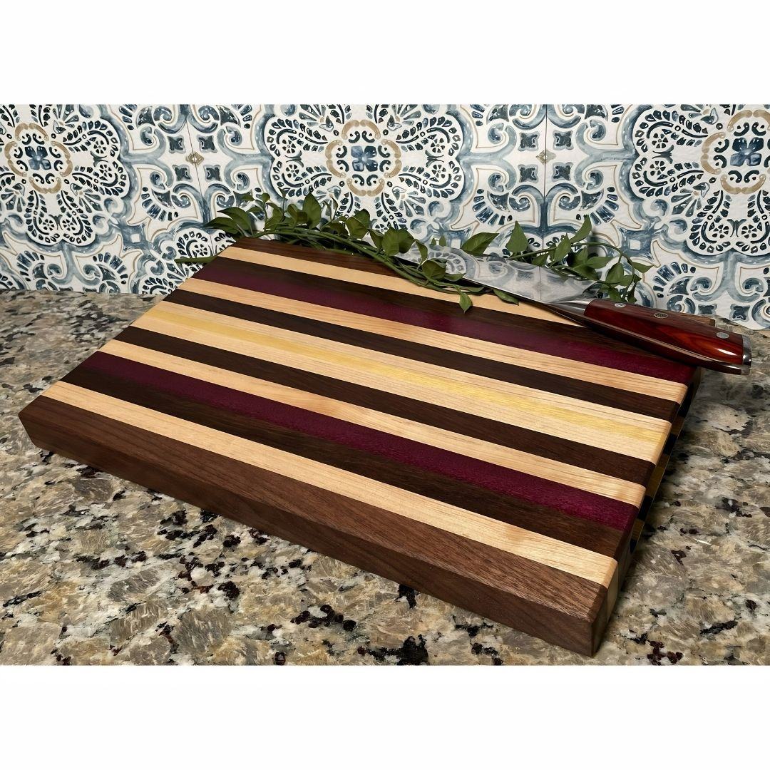 Edge grain cutting board with purpleheart and osage orange stripes on a kitchen counter