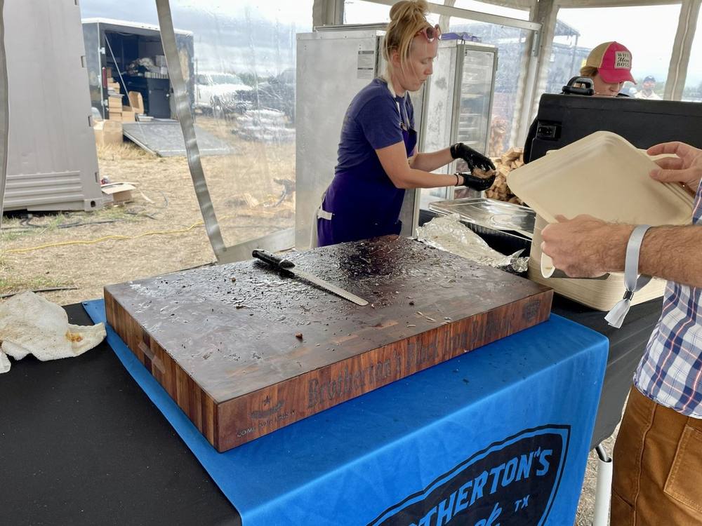 Brotherton's Black Iron Barbecue serving from their end grain butcher block in a festival tent, with the name along the side