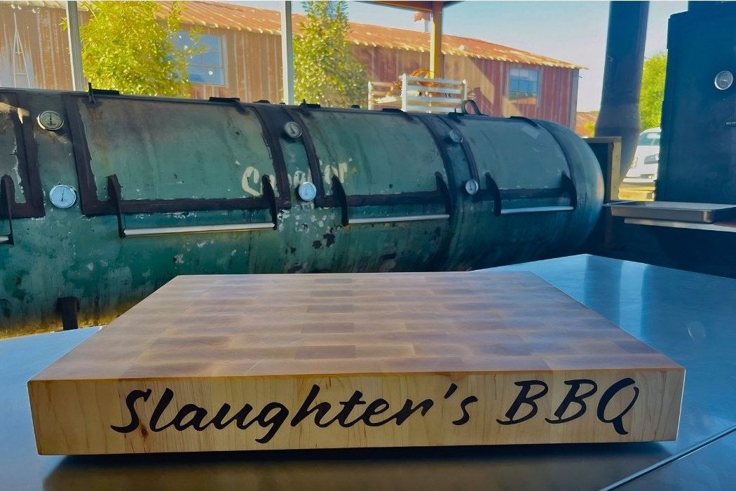 Slaughter's BBQ hard maple end grain butcher block with the name inlaid in script along the side, in front of their offset smoker