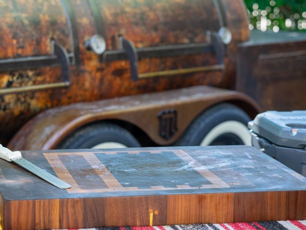 Walnut end grain butcher block built for Brendan Lamb, with a contrasting hardwood pattern, set up in front of a rusted offset smoker